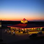 Eine Buc-ee's Tankstelle mit einem roten Dach und einem leuchtenden "Buc-ee's"-Schild bei Sonnenuntergang.